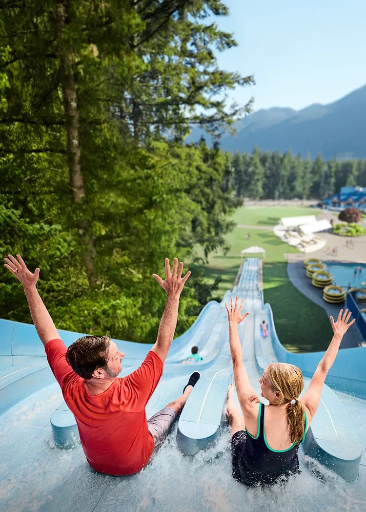 A man and a woman holding their hands up as they go down a water slide