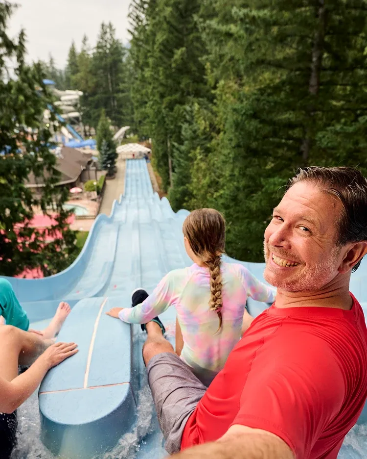 A man taking a selfie at the top of a water slide with his daughter