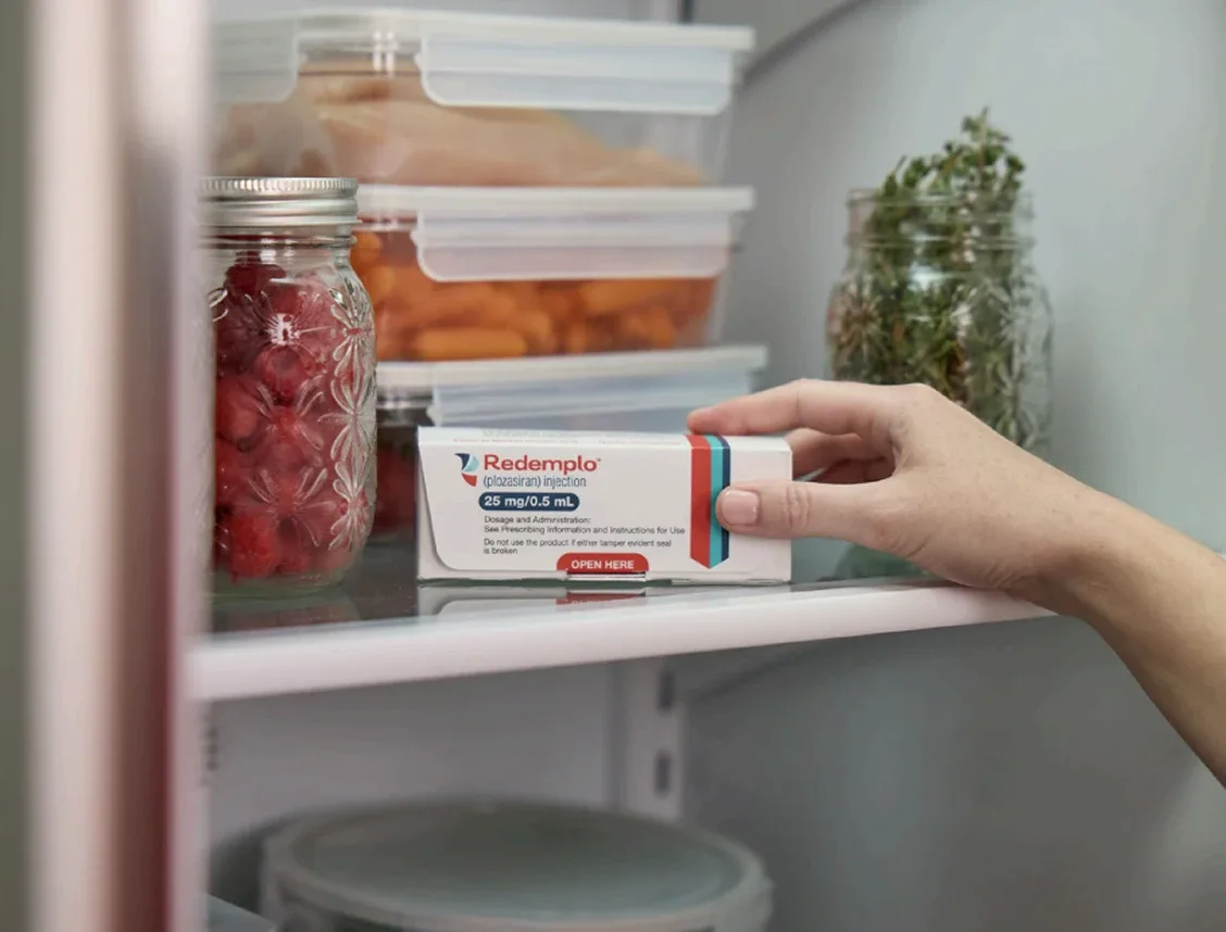 A hand grabbing their packaged Redemplo® (plozasiran) medication from their fridge